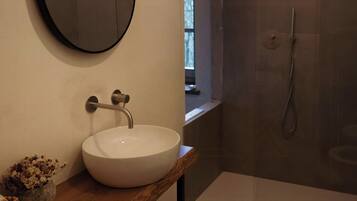 Ein Badezimmer mit rundem Spiegel, Waschbecken in Weiß, Dusche und Toilette.
