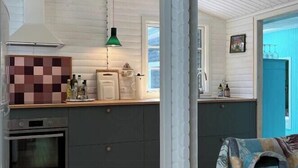 A kitchen with a stove, oven, and a hanging green light fixture. - Colourful summerhouse close to Vig (Vig)