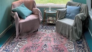 A room with two armchairs, a small table, a patterned rug, a window with a view of greenery, and a wall-mounted lamp. - Colourful summerhouse close to Vig (Vig)
