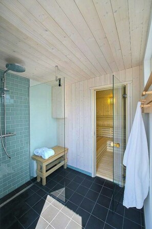 Ein modernes Badezimmer mit Holzboden, einer Duschkabine aus Glas, einer Sitzbank und einem Handtuchhalter.