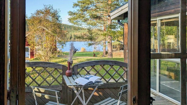 Una terraza de madera con una mesa y sillas, con vista a un lago y árboles.