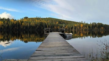 Un muelle de madera se extiende sobre aguas tranquilas, rodeado de un bosque frondoso con follaje otoñal.