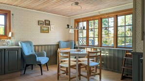 Un cuarto acogedor con techo de madera, una ventana con vista a árboles, una mesa con sillas y un sillón azul.