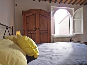 Ein Schlafzimmer mit einem Bett, einem Holzschrank und einem Fenster mit geöffnetem Klappladen.