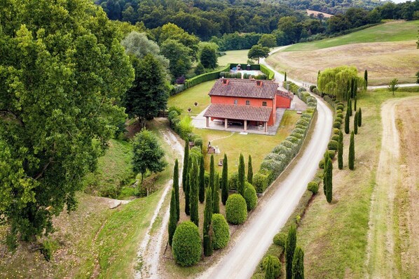 A rural house with a red roof, surrounded by a well-maintained garden and a winding road. - Large villa with pool and sauna on Tuscan estate (Reggello)