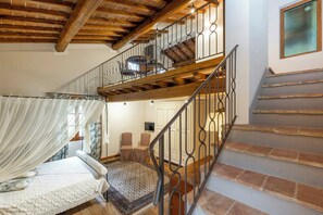 A bedroom with a canopy bed, a staircase with a wrought iron railing, and a view of the living area. - Large villa with pool and sauna on Tuscan estate (Reggello)