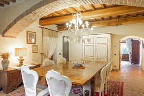 A dining area with a wooden table, white chairs, a chandelier, and a brick ceiling. - Large villa with pool and sauna on Tuscan estate (Reggello)