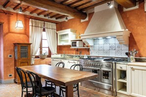 A kitchen with a wooden table, chairs, a stove, oven, and cabinets. - Large villa with pool and sauna on Tuscan estate (Reggello)