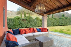 An outdoor seating area with a sofa and chairs, a pergola overhead, and a view of a well-maintained hedge and lawn. - Large villa with pool and sauna on Tuscan estate (Reggello)