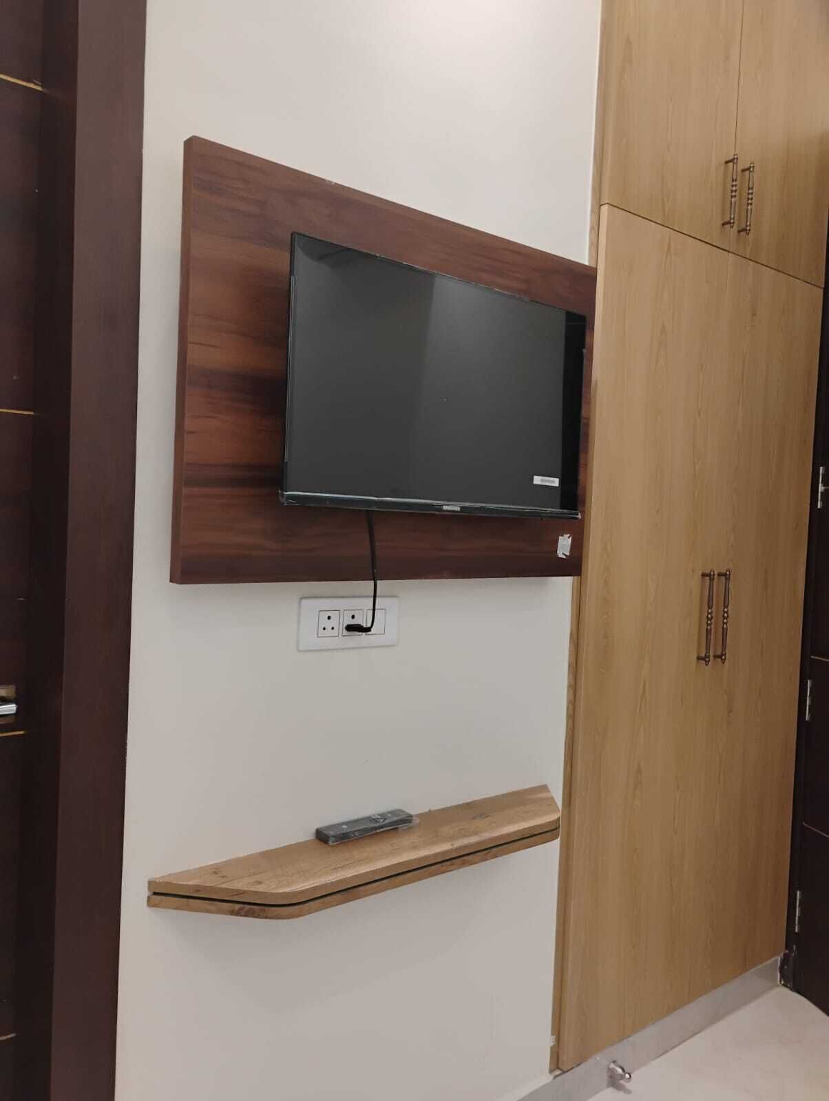 Un téléviseur fixé au mur, avec une étagère en bois en dessous.