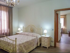 Ein Schlafzimmer mit einem Bett, zwei Nachttischen mit Lampen, einer Chandelüster und einer Tür zu einem anderen Raum.
