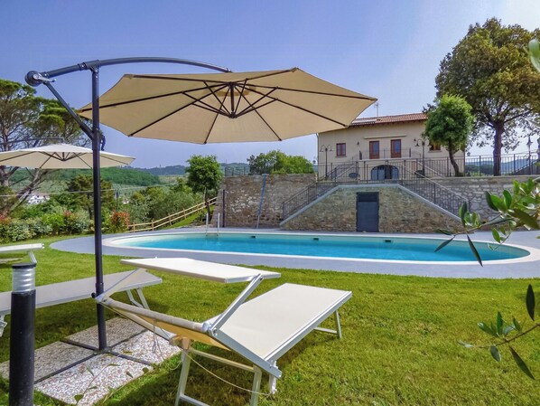 Ein Pool mit Liegestühlen und Sonnenschirmen, umgeben von einer Steinmauer und einem Gebäude mit rotem Dach.