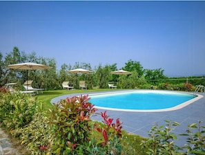 Ein Schwimmbad mit Liegestühlen und Sonnenschirmen, umgeben von viel Grün.