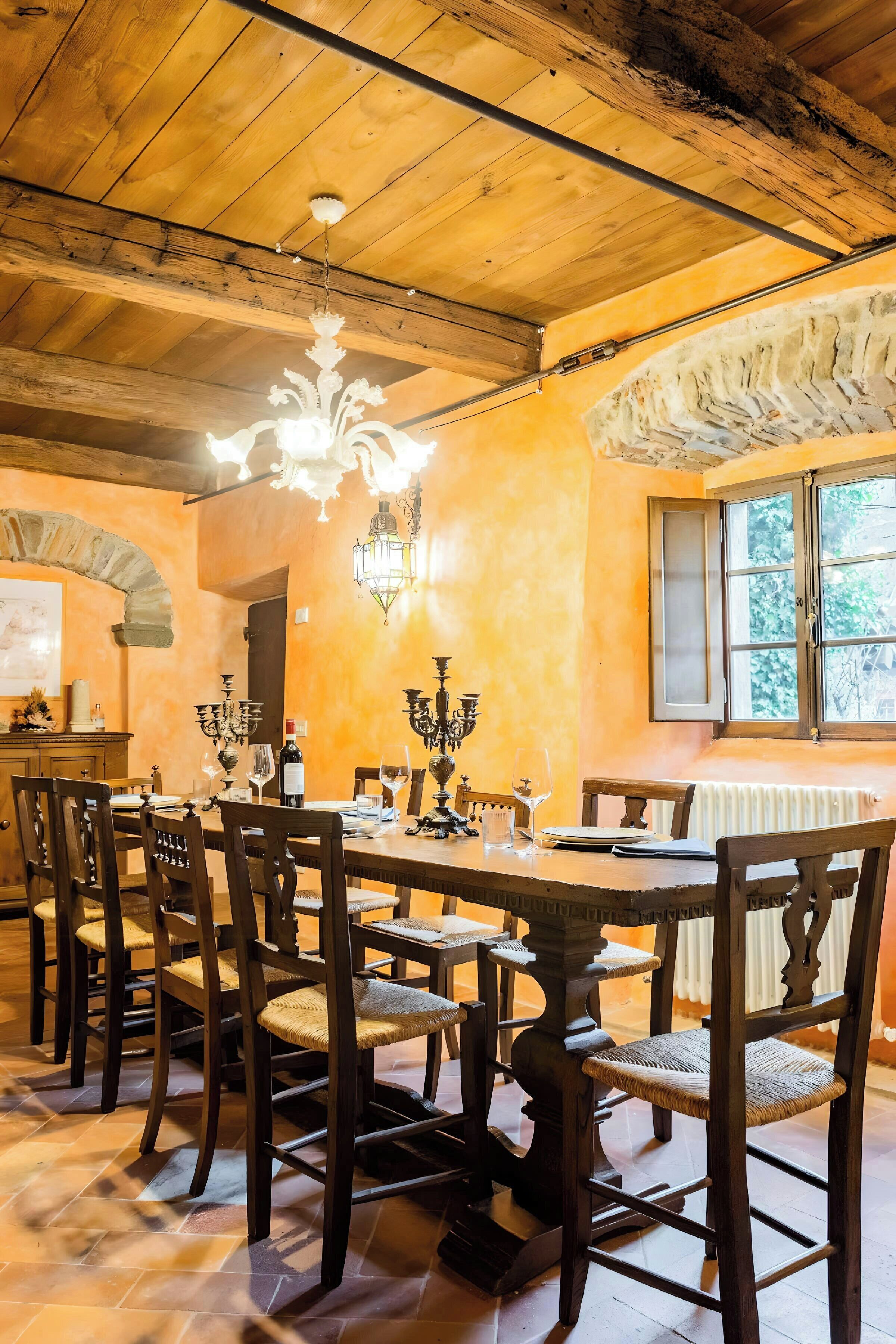 Zona pranzo con tavoli e sedie in legno, un lampadario e una finestra vista.