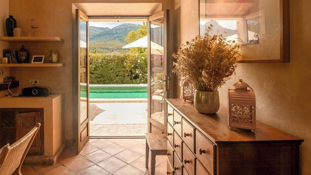 Un couloir menant à une piscine avec vue sur les montagnes, agrémenté de meubles en bois et d’objets décoratifs.