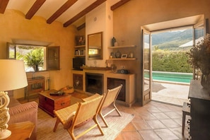 Ein Wohnzimmer mit Kamin, einem Essbereich und Blick auf eine grüne Landschaft durch eine offene Tür.