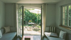 Een open woonkamer met een bank, een eettafel met stoelen en uitzicht op de tuin door een glazen deur.