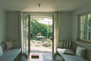 An open-plan living area with a sofa, a dining table with chairs, and a view of the garden through a glass door. - Riverside Studio with Garden Views (Werder (Havel))