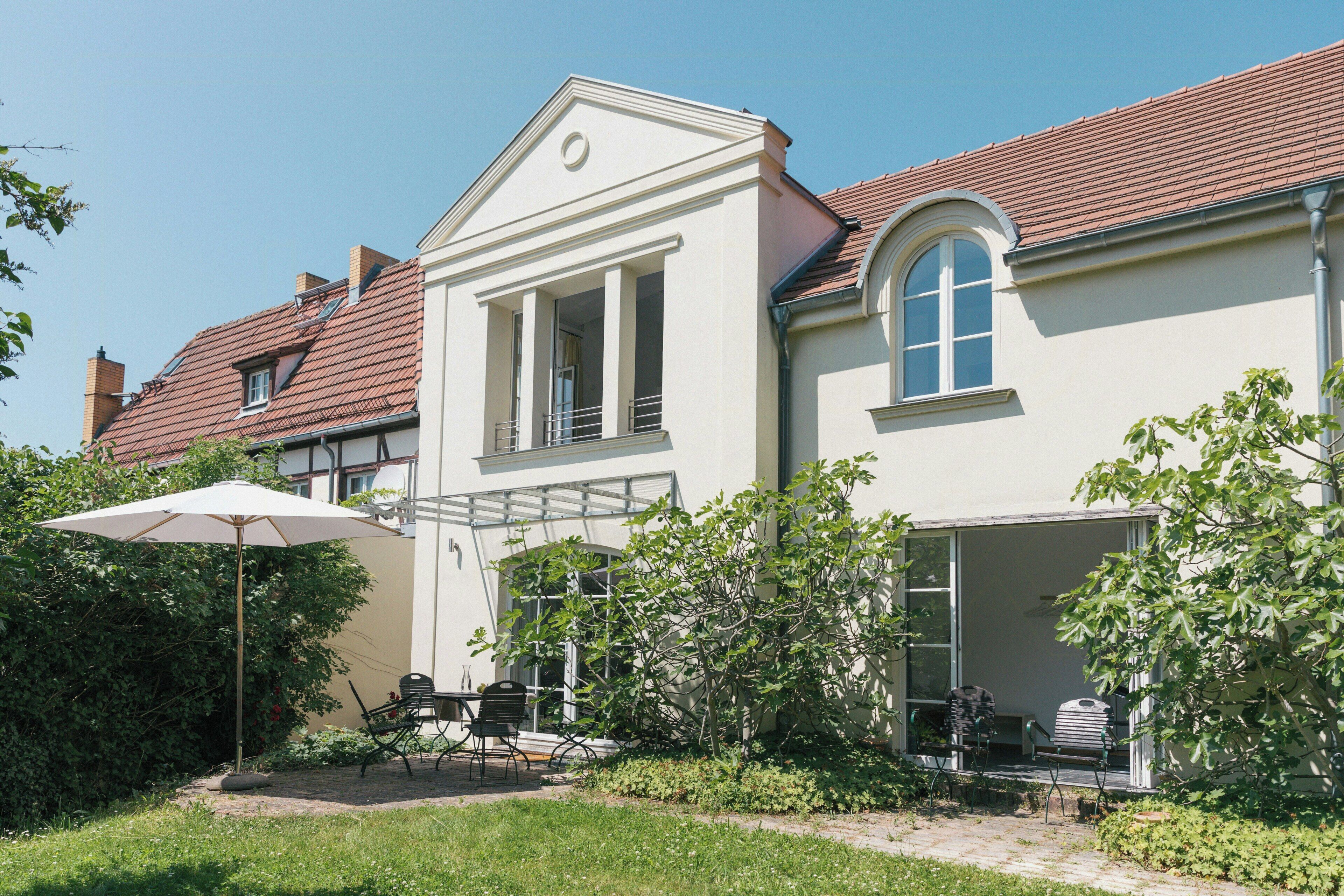 Ein zweistöckiges Haus mit überdachter Terrasse, einem kleinen Garten und einer sichtbaren Garage.