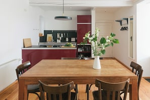 A dining area with a wooden table and chairs, a vase with flowers, and a kitchen in the background. - Riverside Studio with Garden Views (Werder (Havel))