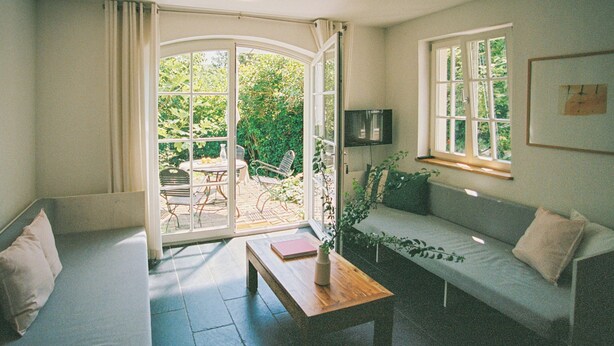Een kamer met een bank, een tafel, een houten bankje, een televisie en een raam.