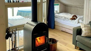 A cozy room with a wood-burning stove, a bed, a sofa, and a view of the outdoors. - Cottage with beach access on Sjællands Odde (Sjællands Odde)