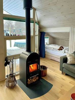 Ein gemütliches Zimmer mit Kamin, einem Bett, einer Couch und Blick ins Freie.