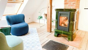 A loft-style room with a green wood-burning stove, a blue armchair, and a geometric-patterned rug.