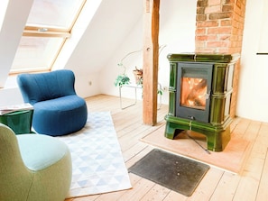 A loft-style room with a green wood-burning stove, a blue armchair, and a geometric-patterned rug. - Spacious country house with idyllic orchard (Schönwalde)