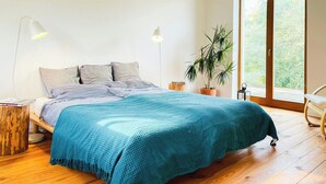 A bedroom with a bed, two bedside lamps, a potted plant, and a sliding glass door to the outside.