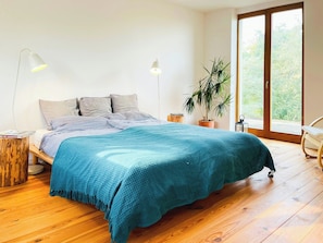 Ein Schlafzimmer mit einem Bett, zwei Nachttischlampen, einer Topfpflanze und einer SchiebetĂŒr zum AuĂenbereich.