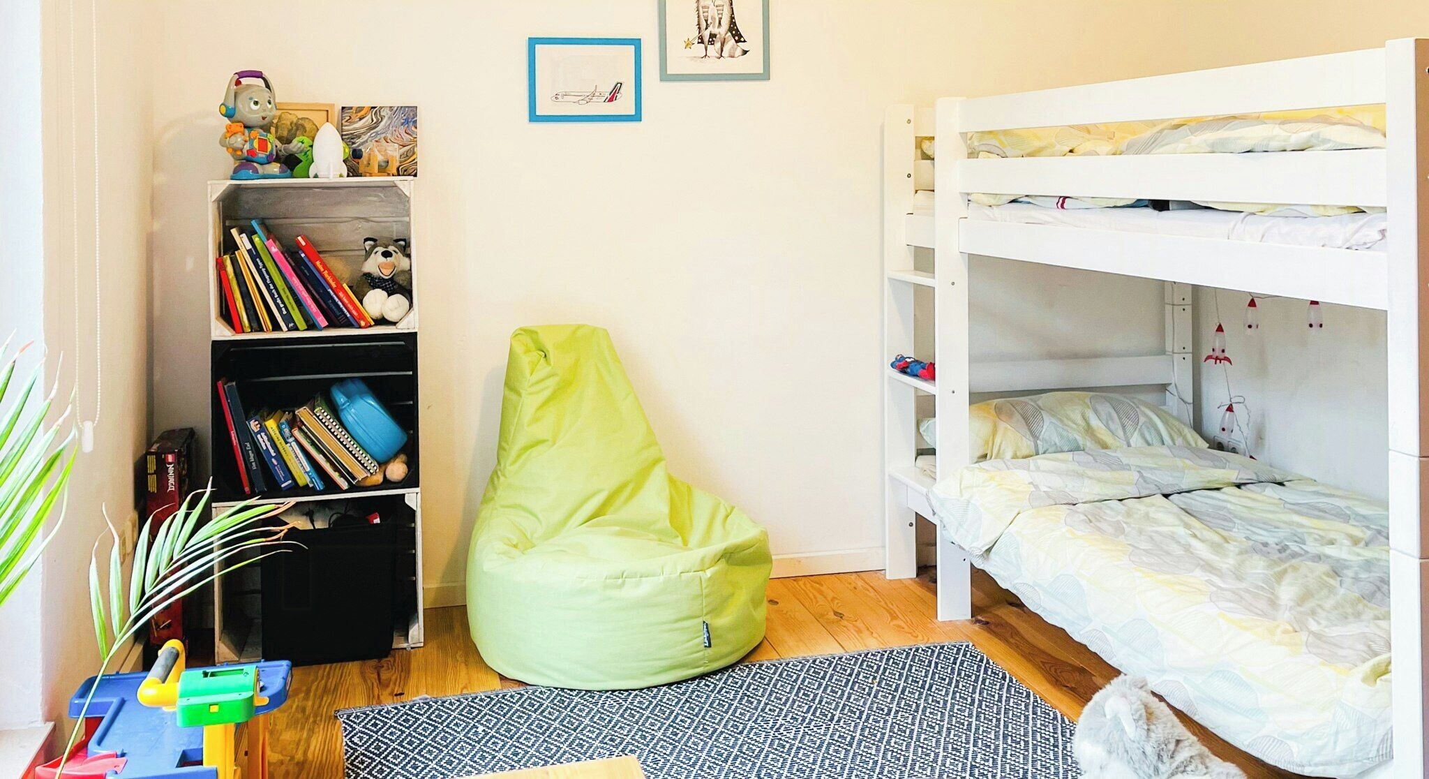 Una habitación infantil con una cama litera, una estantería, un sillón de peluche y una alfombra estampada.