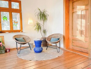 A room with a wooden floor, two wicker chairs, a blue vase, a lamp, and a window with decorative stickers. - Spacious country house with idyllic orchard (Schönwalde)