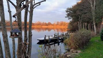 A tranquil lakeside scene with a dock, trees, and a bird feeder.