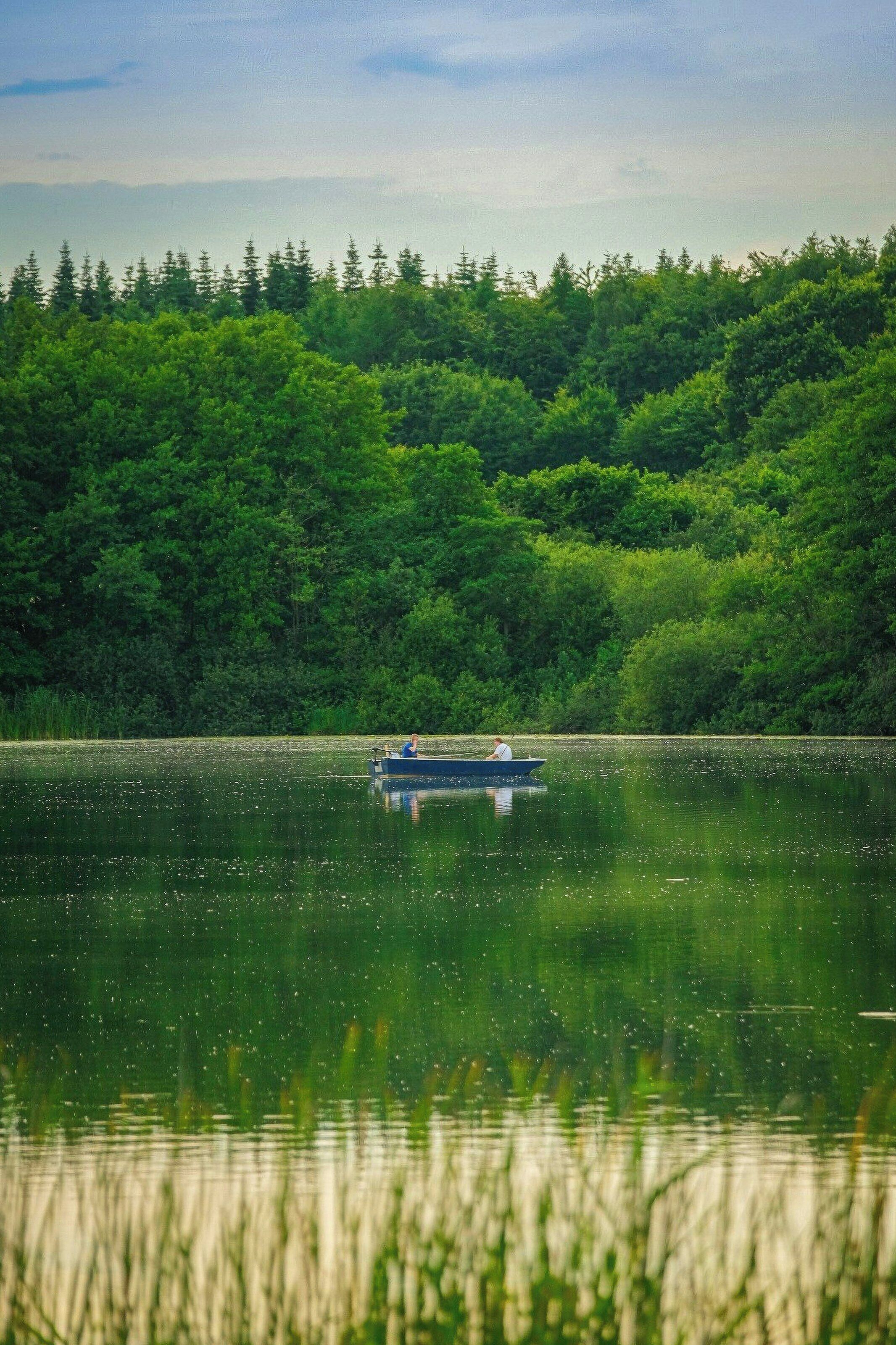 A calm lake with a boat and dense forest in the background.