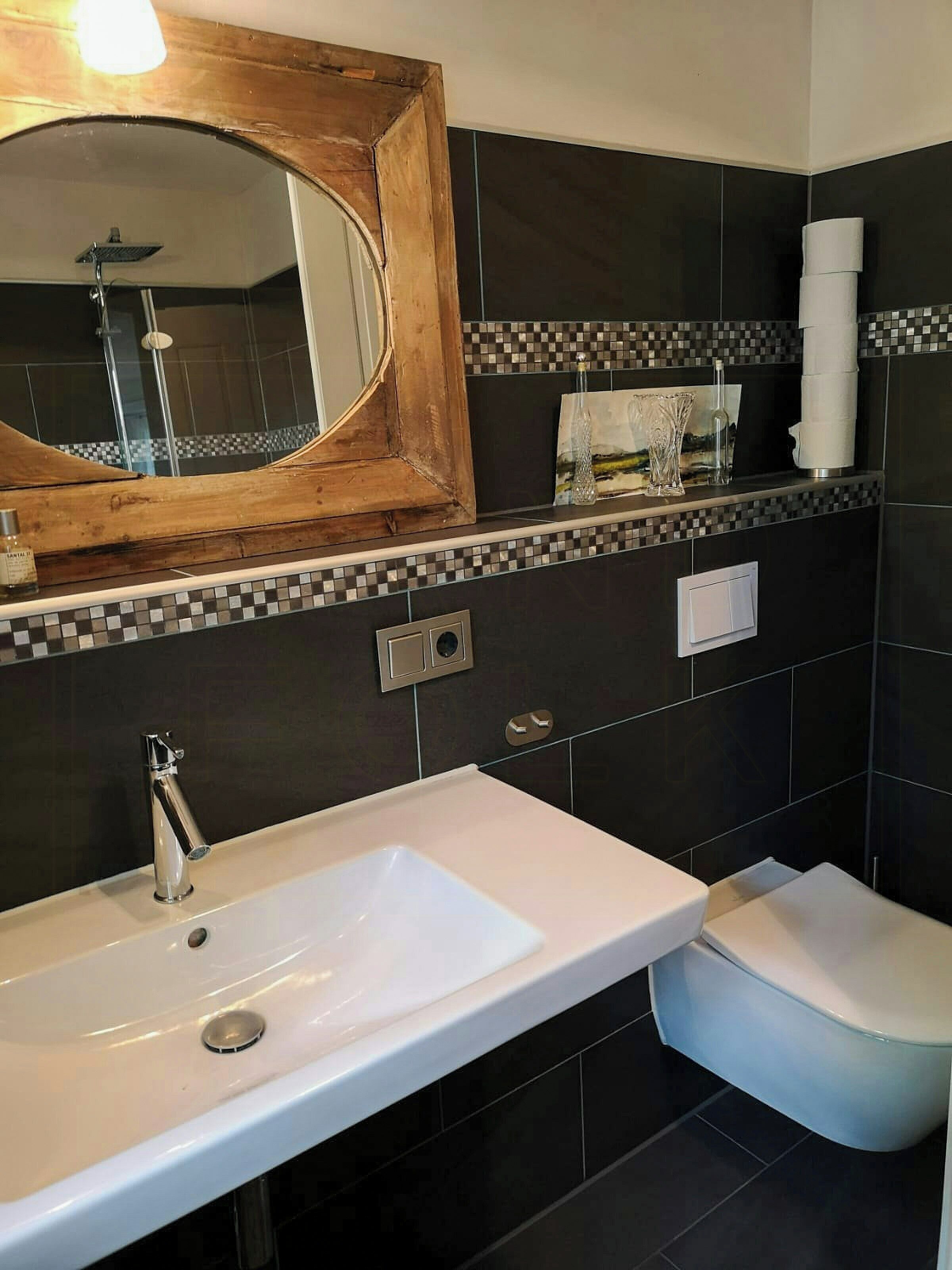 Een badkamer met een wit wastafelmeubel, een spiegel, een douche en een toilet.