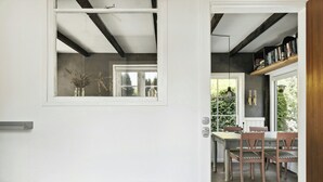 A bedroom with a bed, a window, and a view of a dining area with chairs and a table. - Modern summer house near Udsholt Beach (Græsted)