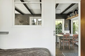 Ein Schlafzimmer mit Bett, Fenster und Blick auf einen Essbereich mit Stühlen und Tisch.