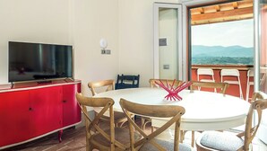Un comedor con una mesa redonda, sillas, un televisor sobre un mueble rojo y vistas a través de un ventanal.