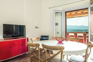 A dining area with a round table, chairs, a TV on a red cabinet, and a view through a glass door. - Apartment with pool and views of Valdarno (Reggello)