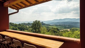 Una barra de madera con sillas, vista a un paisaje verde con árboles y colinas, y un cielo nublado.