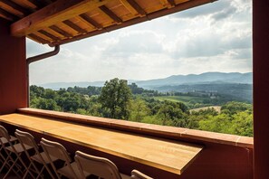A wooden bar with chairs, a view of a green landscape with trees and hills, and a cloudy sky. - Apartment with pool and views of Valdarno (Reggello)