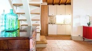 Una escalera lleva a una cocina con armarios blancos, techo de madera y una mesa roja a la derecha.