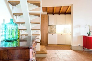 A staircase leading to a kitchen with white cabinets, a wooden ceiling, and a red table on the right. - Apartment with pool and views of Valdarno (Reggello)