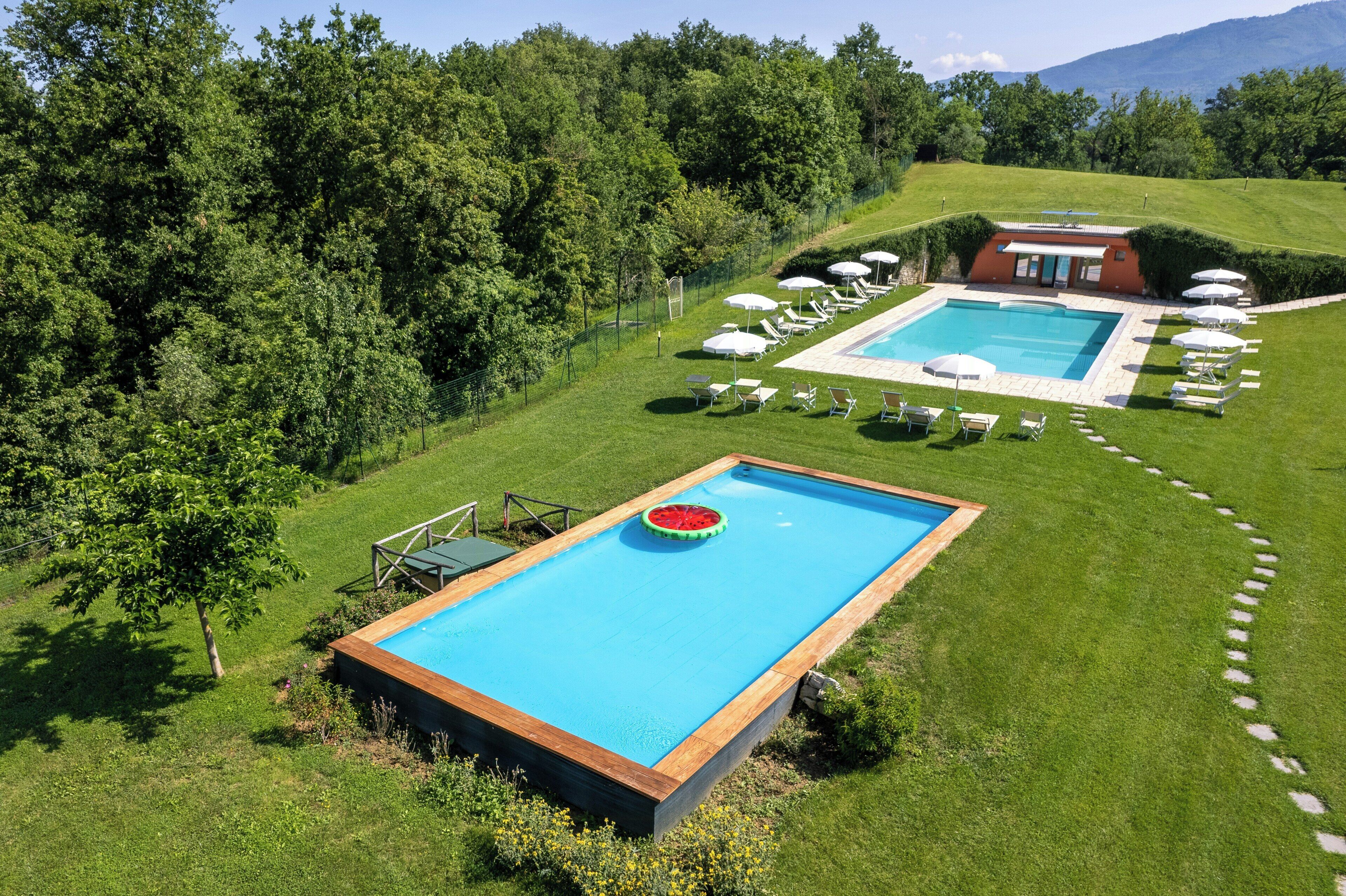 A rectangular pool with a wooden deck, surrounded by a well-maintained lawn and trees.