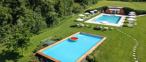 A rectangular pool with a wooden deck, surrounded by a well-maintained lawn and trees.