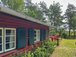 En rød træhytte med grønne skodder, en veranda og udsigt til den omkringliggende skov.