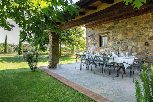 Eine Terrasse im Freien mit Steinmauern, einem Esstisch und einem Baum, der Schatten spendet.