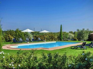 Ein Swimmingpool mit Liegestühlen und Sonnenschirmen, umgeben von viel Grün.