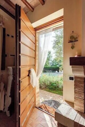 Eine Holztür mit aufgehängtem Handtuch, die zu einem Garten mit einer Steinsitzbank und einem kleinen Tisch führt.